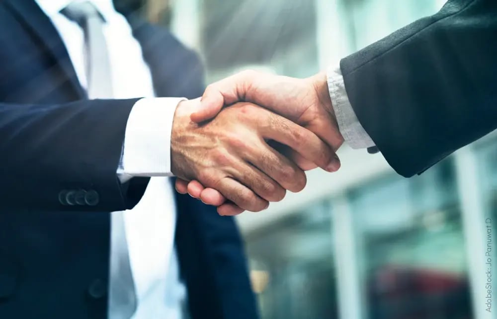 Two male businessmen shake hands after signing a contract.