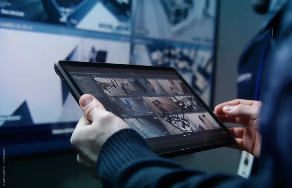 Wachperson hält Tablet und beobachtet CCTV-Bildschirme bei Kameraüberwachung.